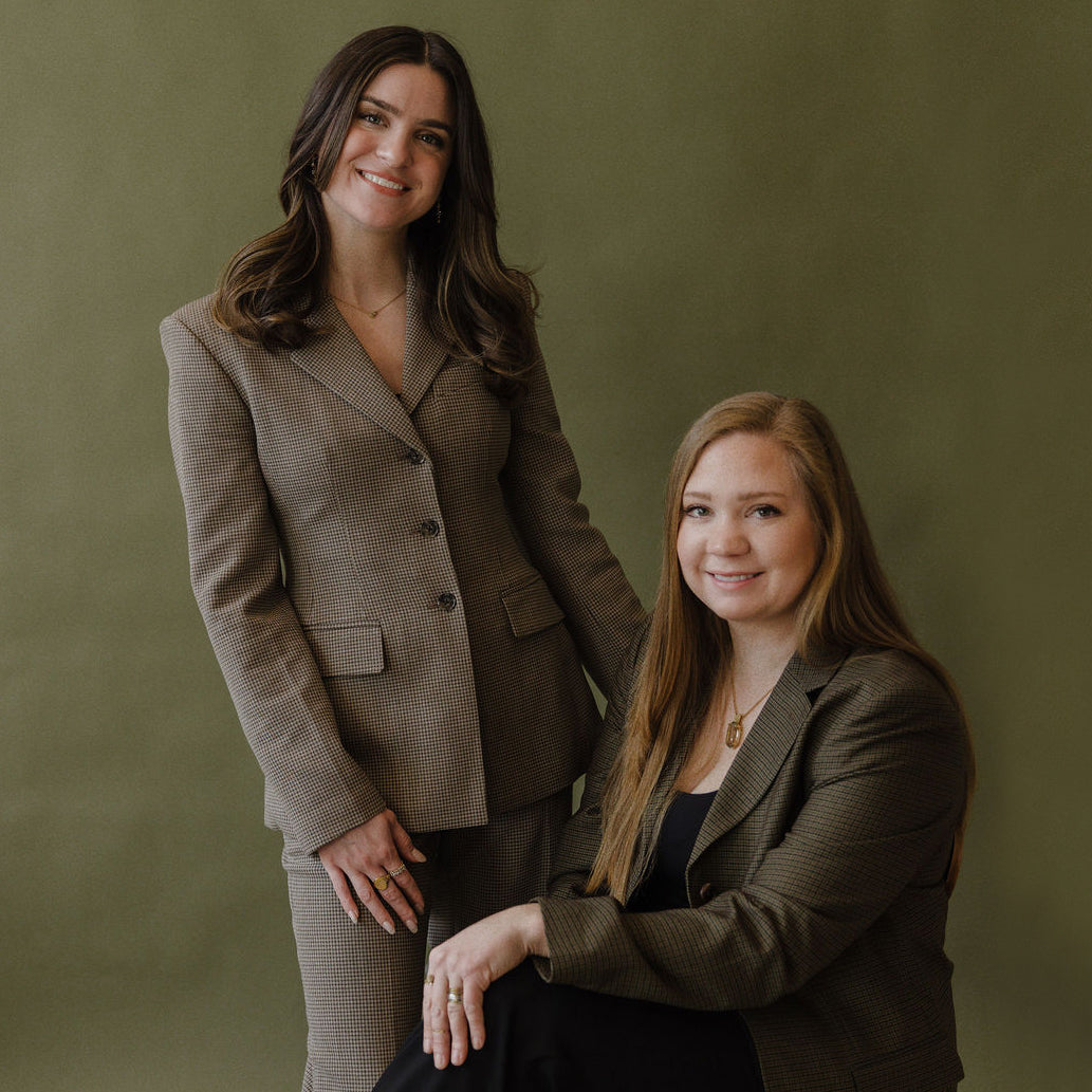 Two women in business attire standing against a green background