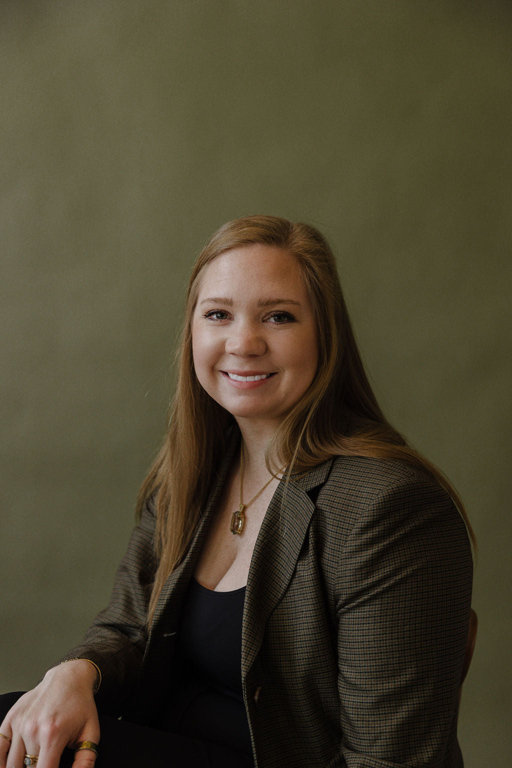 Woman in a green gingham patterned suit sitting against an olive green background