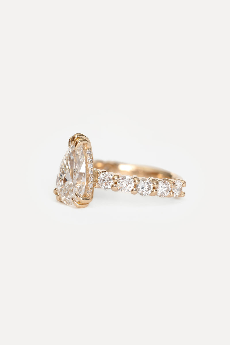 Side view of a yellow gold engagement ring with a pear-shaped lab diamond, hidden halo and pavé band