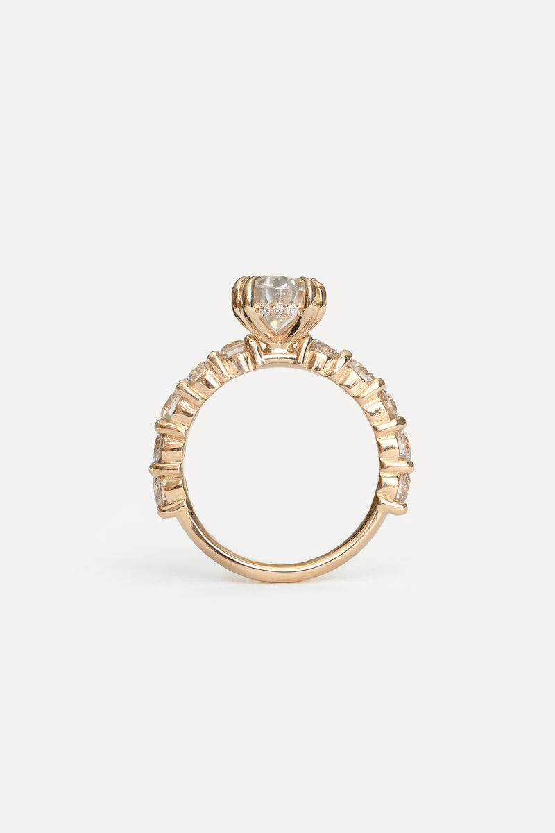 Profile view of a yellow gold engagement ring with a raised main stone, hidden halo and diamonds in the band on a white background