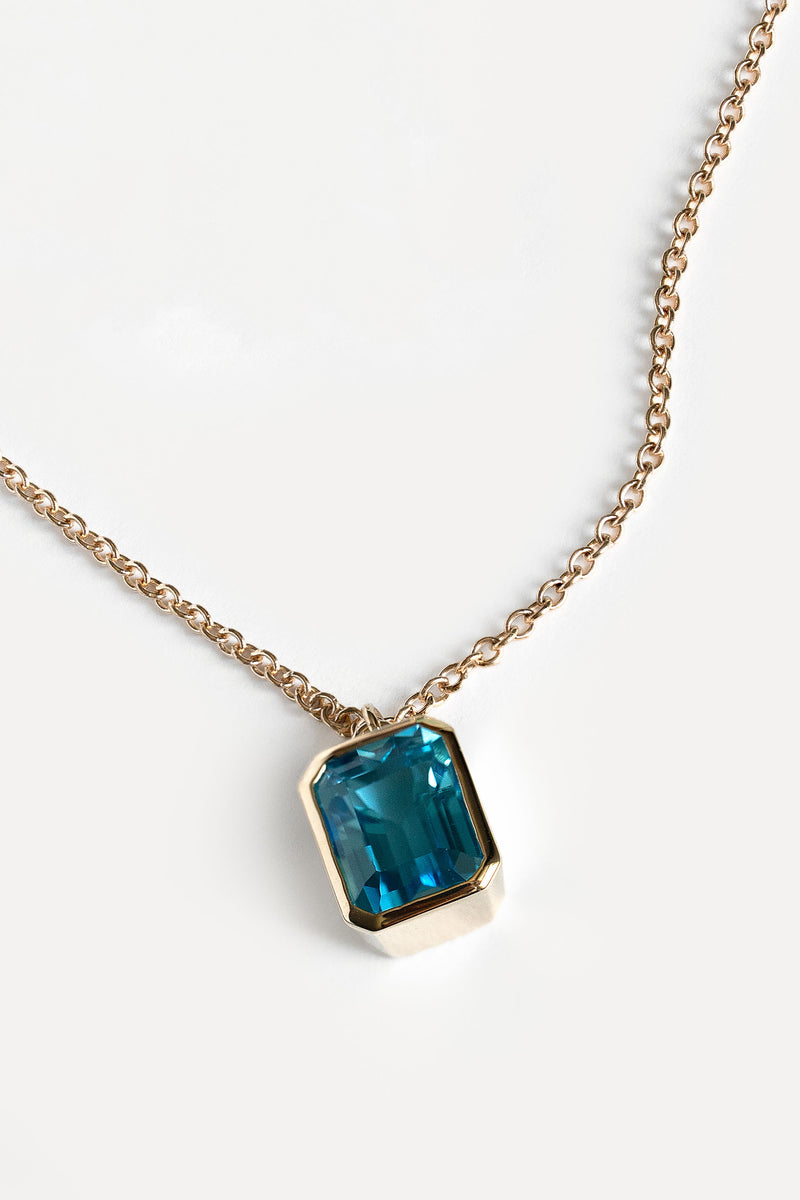 A gold chain necklace with a rectangular blue gemstone pendant in a gold bezel setting, shown on a clean white background.