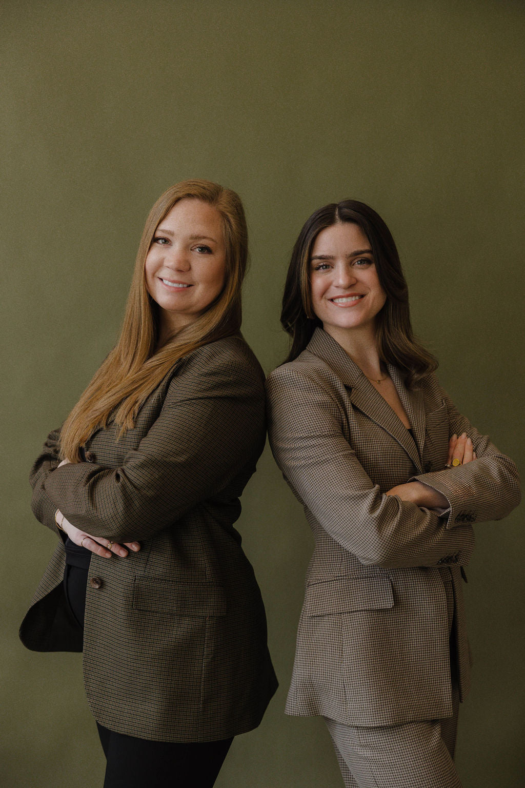 Two women in business suits standing back-to-back against a green background