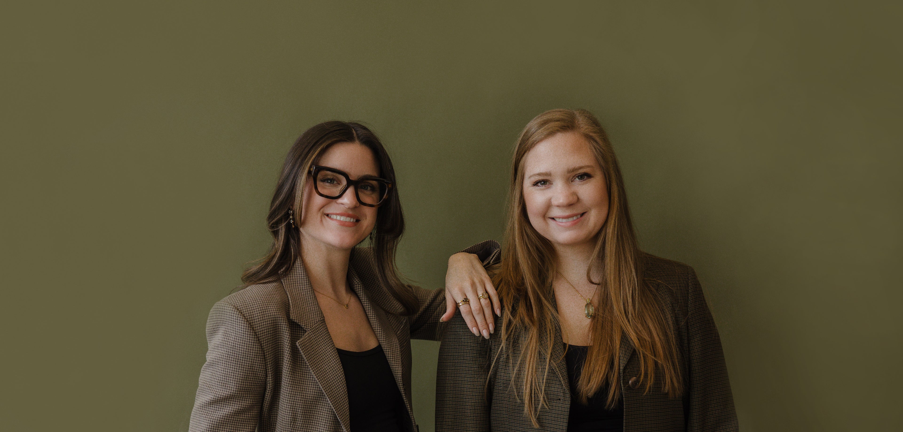 Two women standing side by side against an olive green background