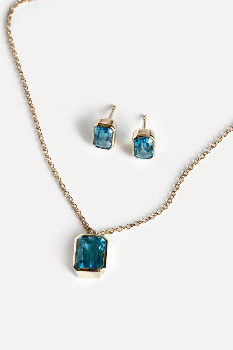 Gold necklace and matching stud earrings with rectangular blue gemstones, displayed on a clean white background.