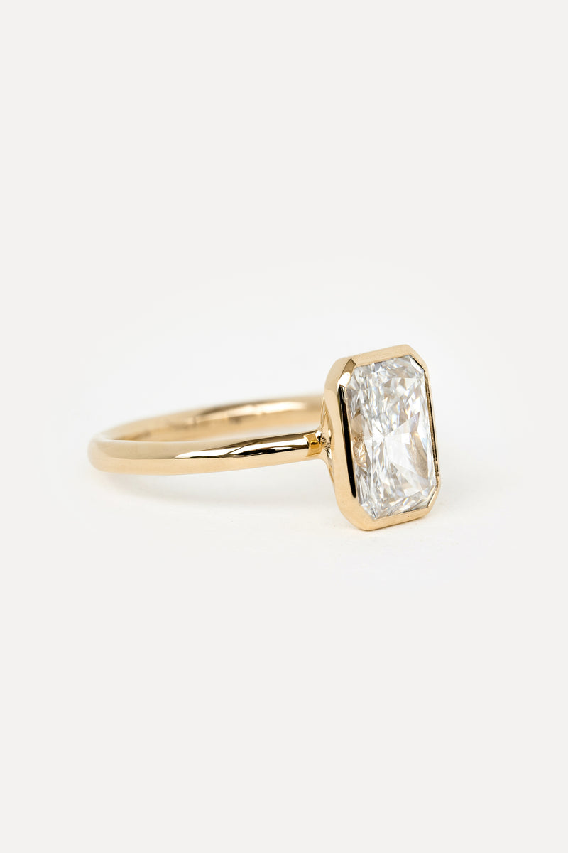 Side view of a solitaire engagement ring in yellow gold with a bezel set radiant cut lab diamond