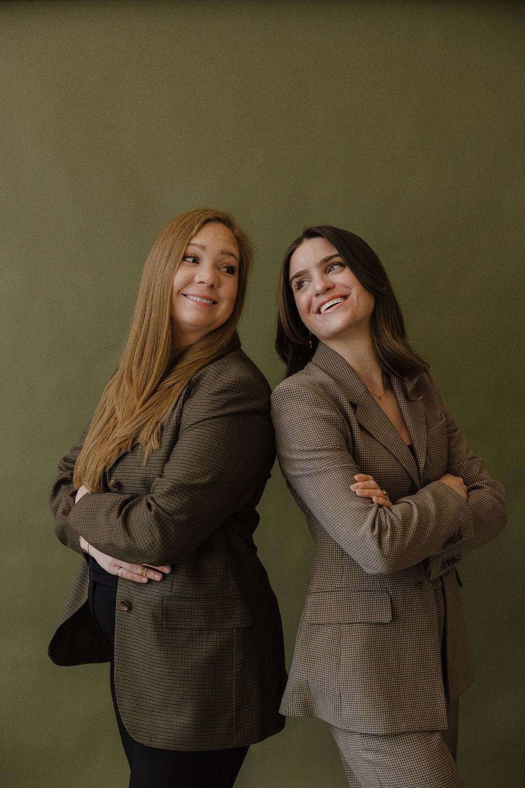 Two women in business attire standing back-to-back against a green background