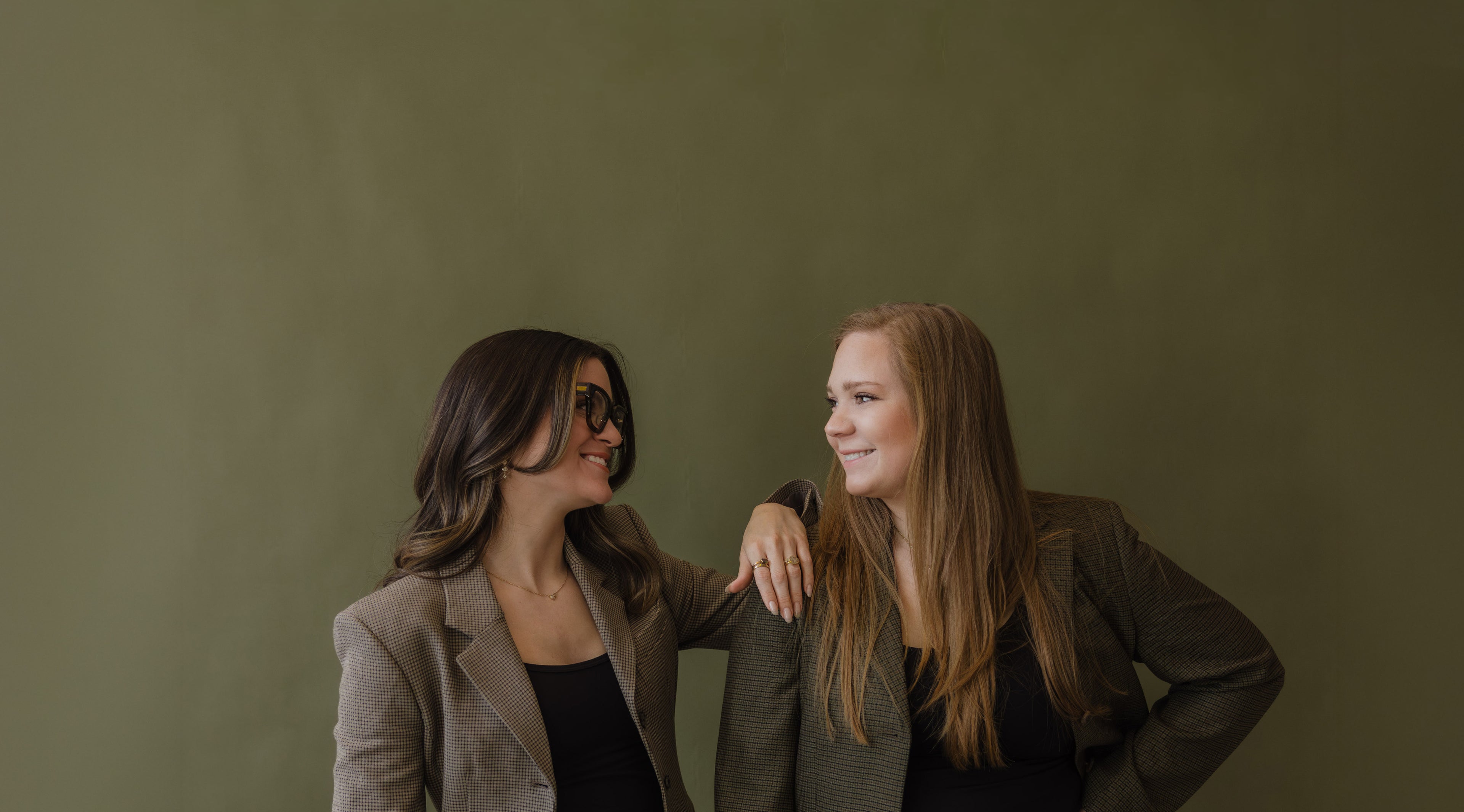 Two women cofounders standing close together against a plain olive green background