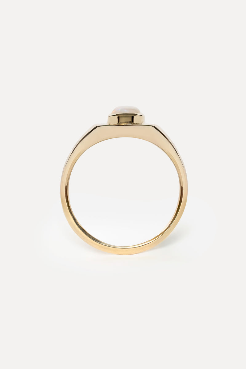 Profile view of a gold ring with a bezel set opal stone on a white background