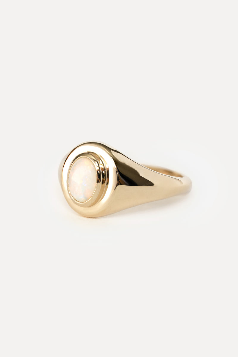 Side view of a gold ring with a bezel set opal stone on a white background