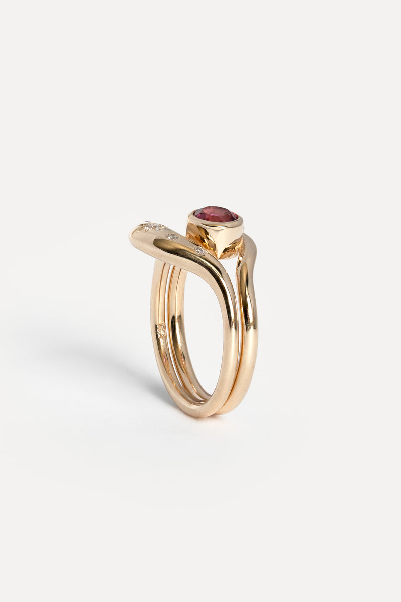 A gold ring with a twisted band design, a small diamond on one side, and a round red gemstone on top, shown on a light gray background.