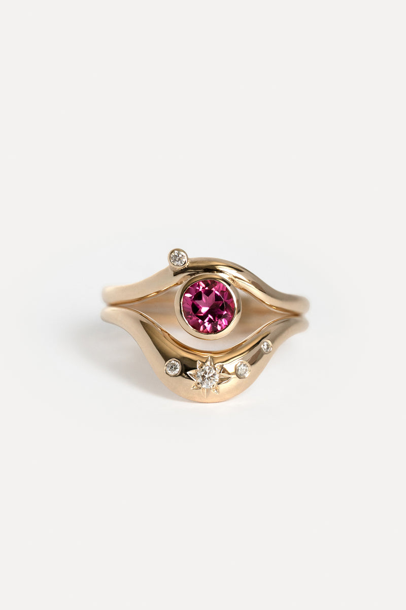 A gold ring featuring a central round pink gemstone surrounded by a wavy gold setting with small clear accent stones, photographed on a clean white background.