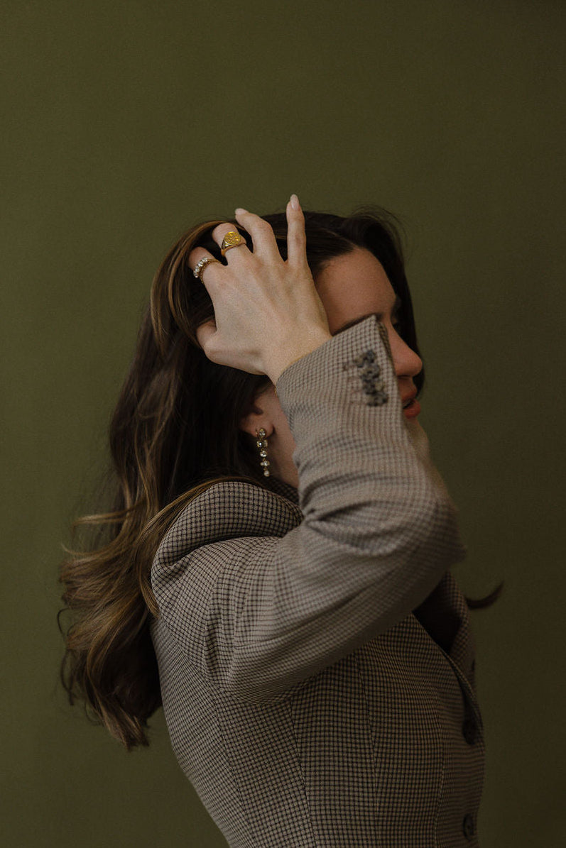 Woman wearing jewelry adjusting her hair against a dark green background